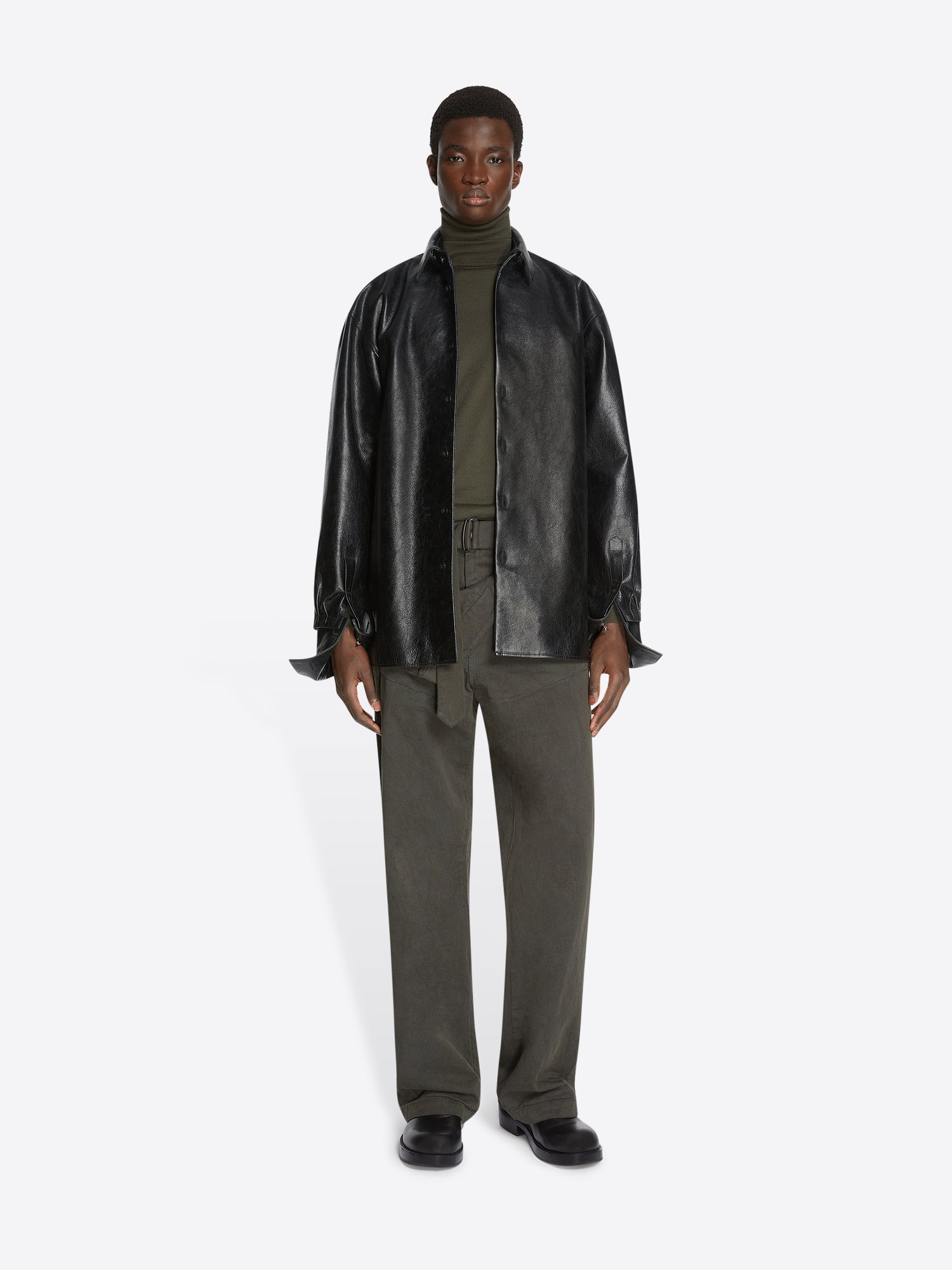 Person wearing a black leather shirt and green pants on a white background