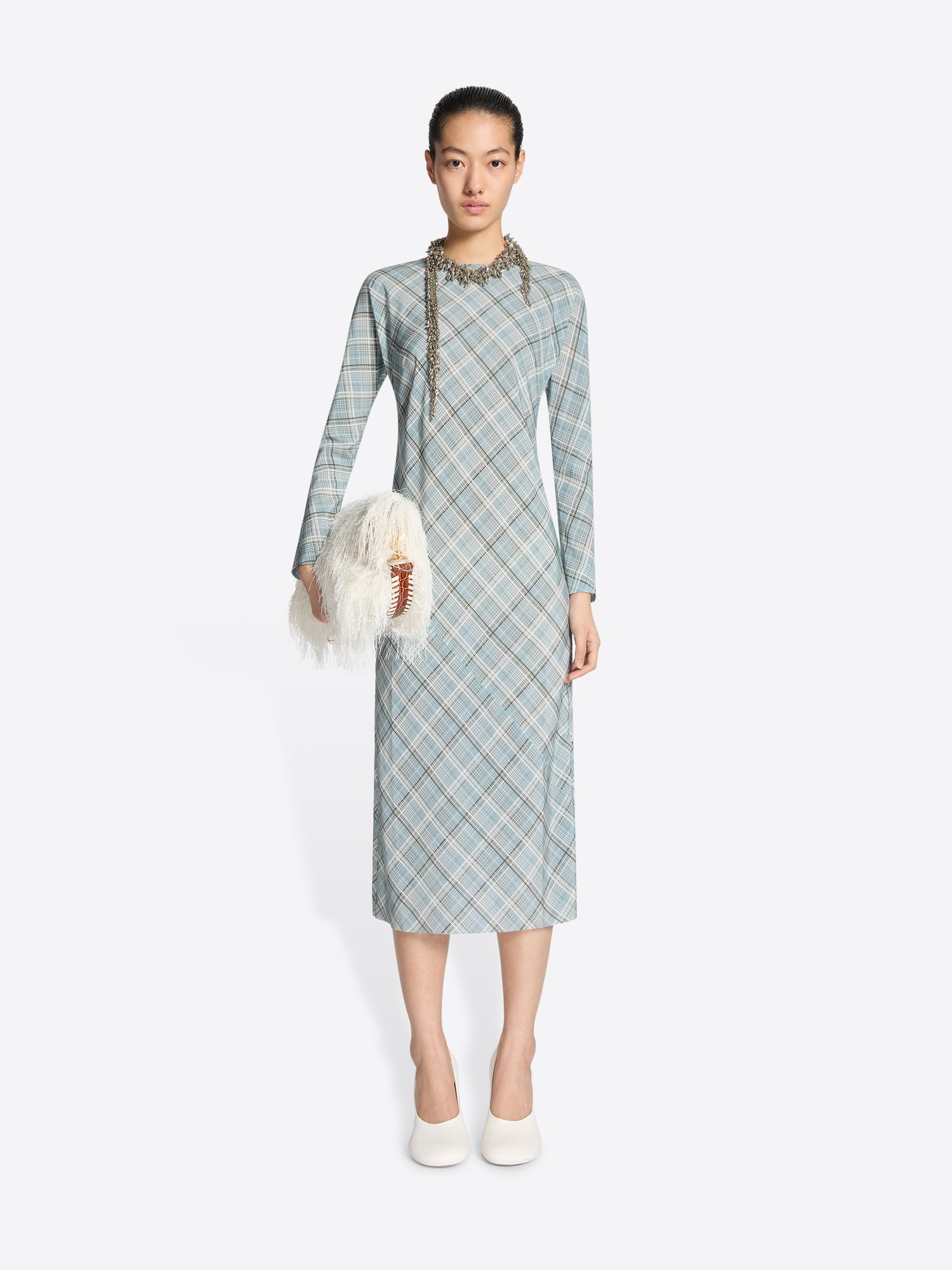 Woman wearing a light blue plaid dress holding a white fur bag on a white background