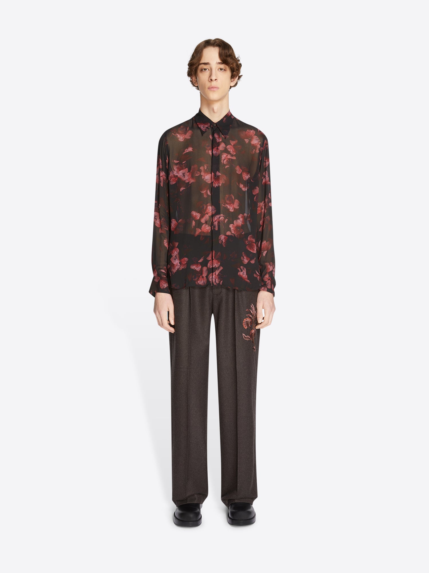 Person wearing a black floral shirt and dark pants on a white background
