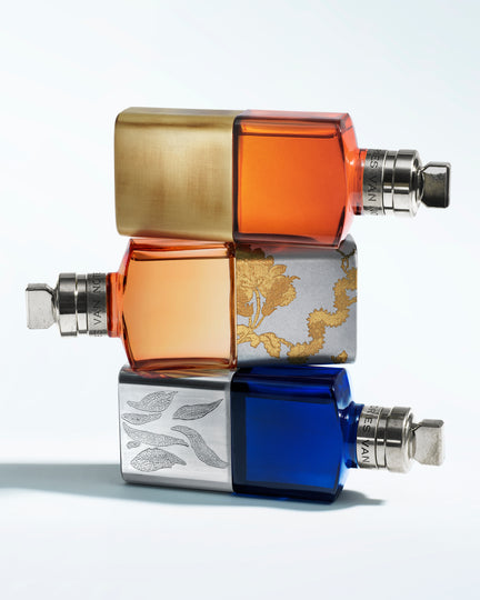 Three stacked perfume bottles with gold, orange, and blue colors on a white background