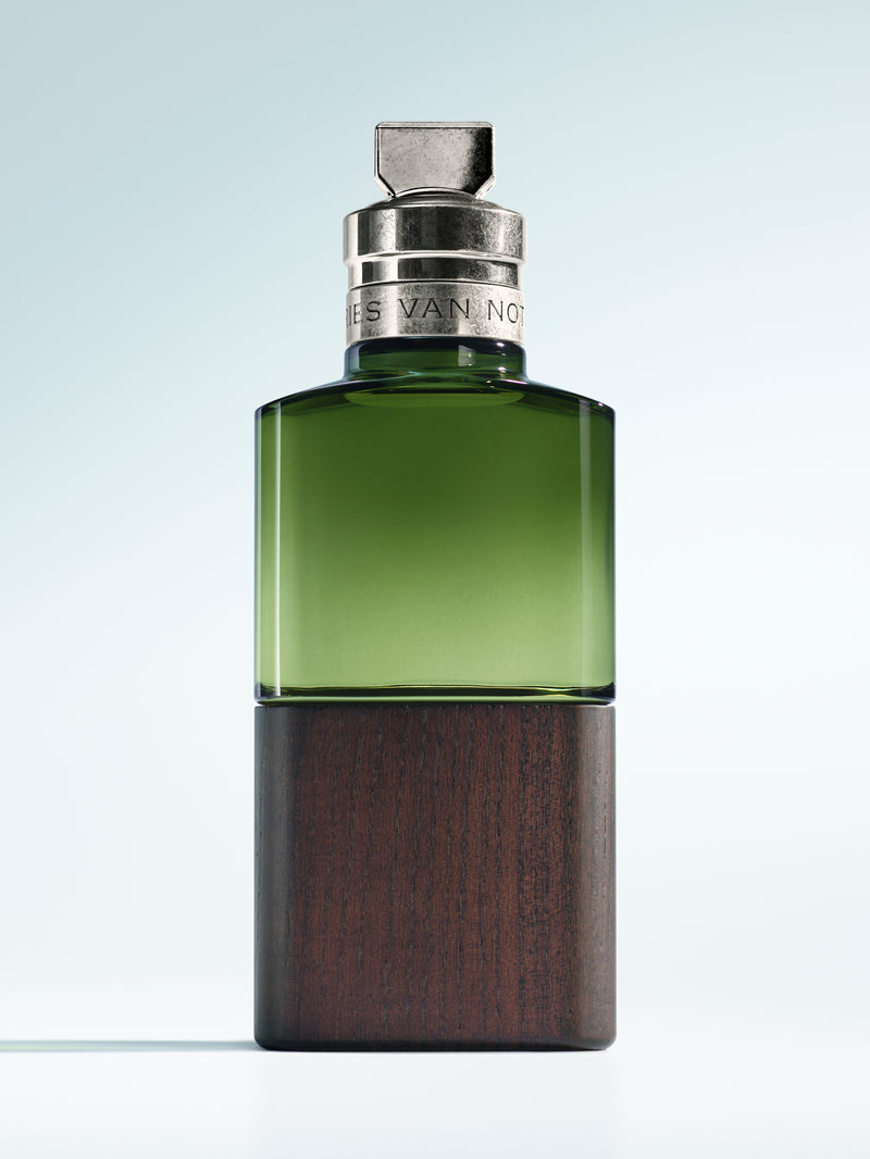 Green and brown perfume bottle with silver cap on a light gray background