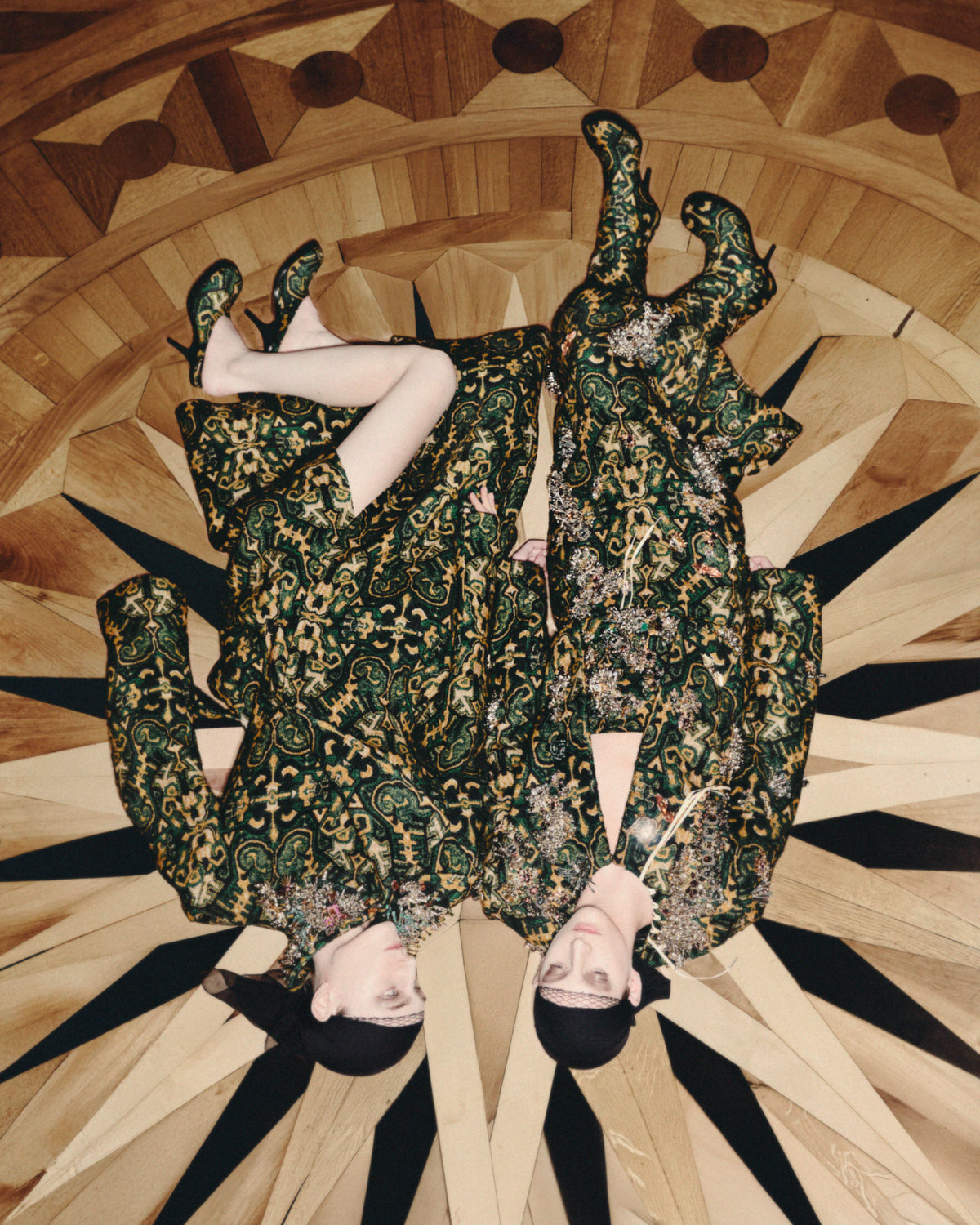 Person wearing a patterned dress lying on a wooden floor with a mirror effect.