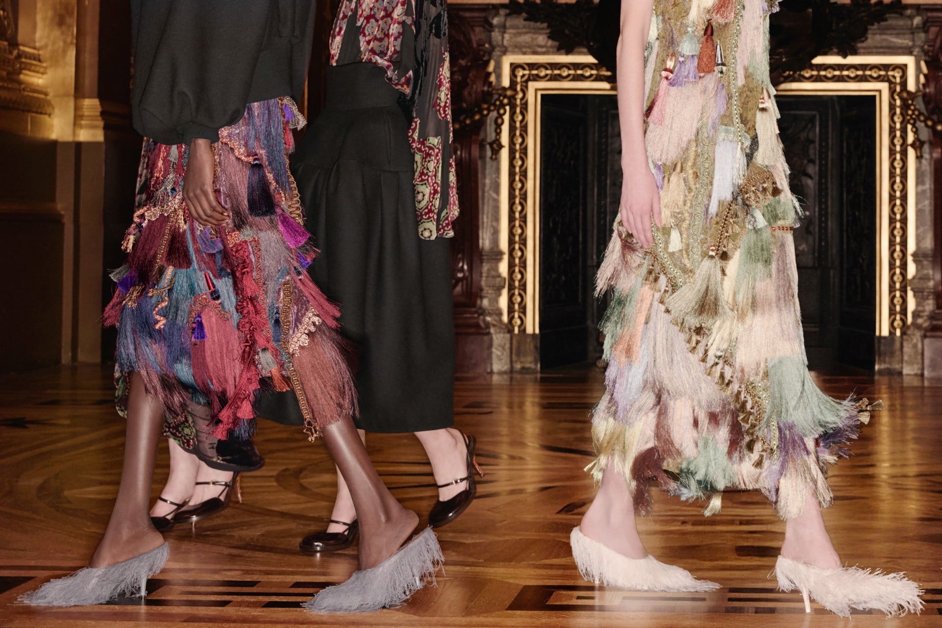 Two models wearing colorful, layered dresses on a wooden floor with decorative background