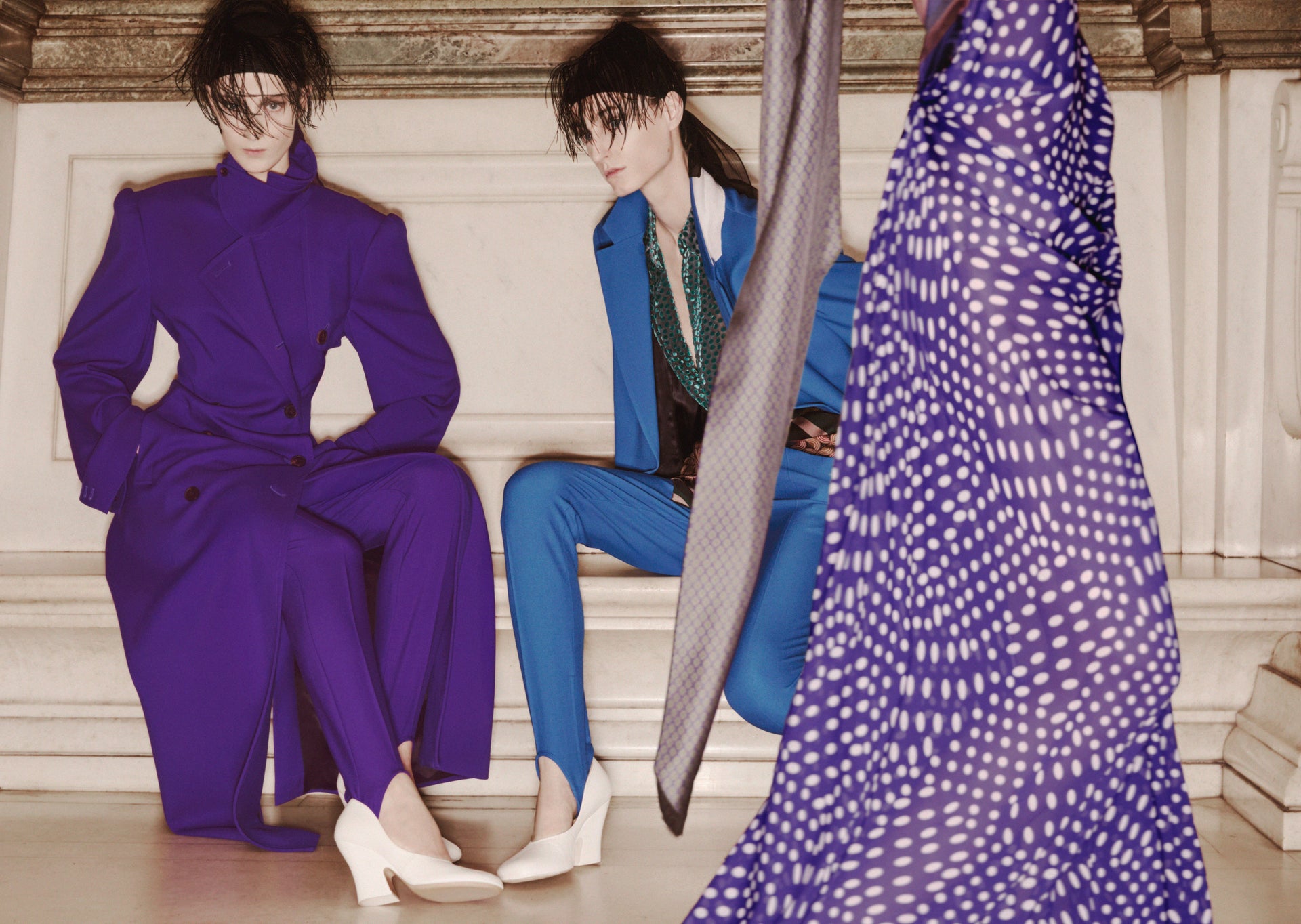 Two women in colorful outfits sitting on a staircase with a patterned fabric in the foreground.