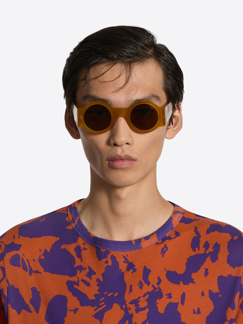 Person wearing round sunglasses with a colorful patterned shirt on a white background
