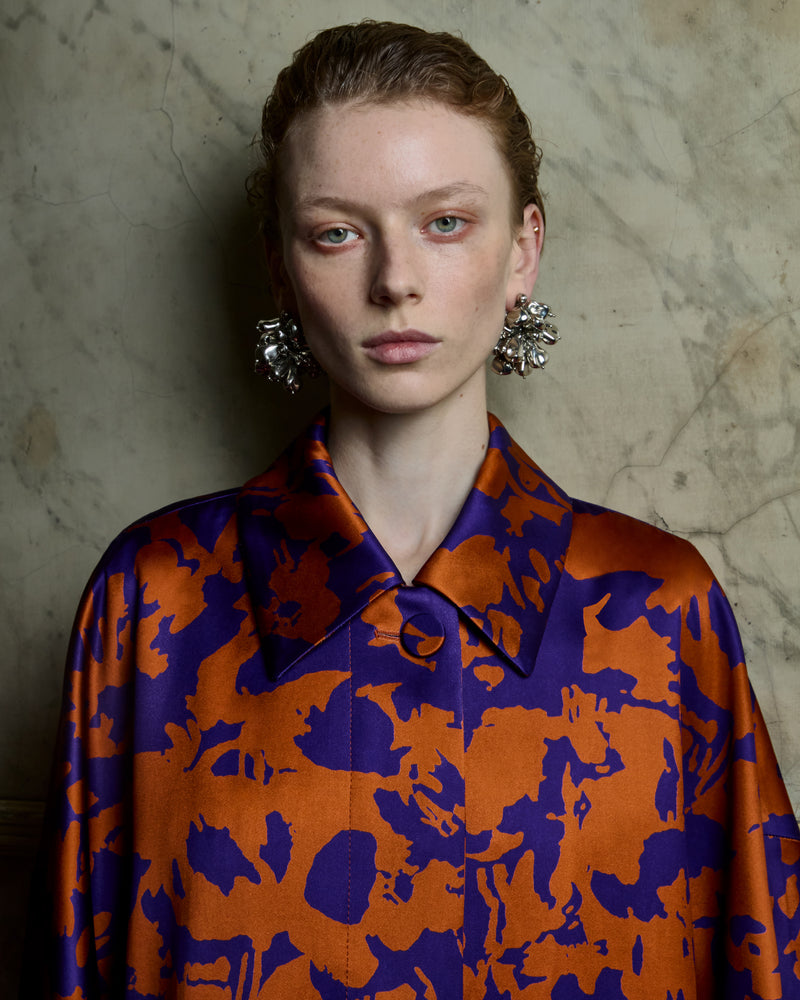 Woman wearing a patterned coat and silver earrings on a grey backround.