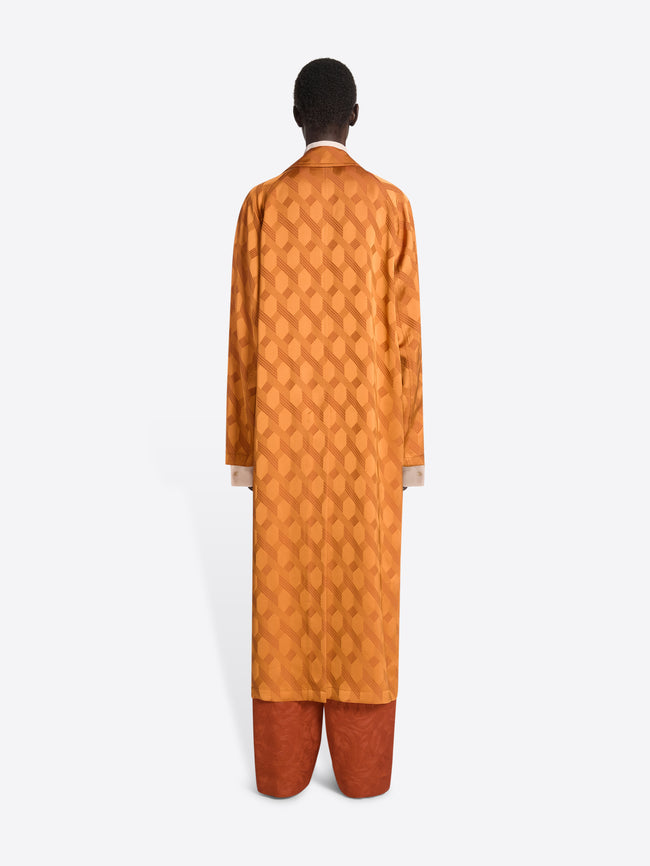 The backside of a person wearing dark orange pants and an orange jacquard mac with chain motif on a white background