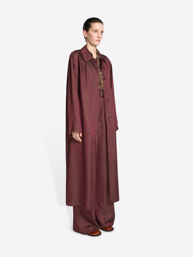 Model wearing a burgundy jacquard mac with tie motif on a white background