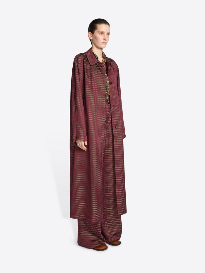 Model wearing a burgundy jacquard mac with tie motif on a white background