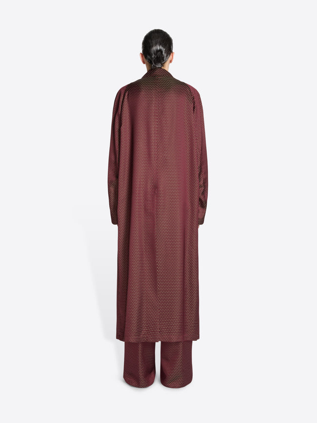 Backside of a model wearing a burgundy jacquard mac with tie motif on a white background