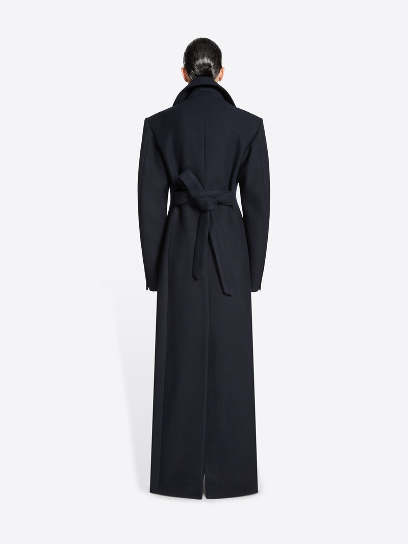 Person wearing a long navy coat on a white background