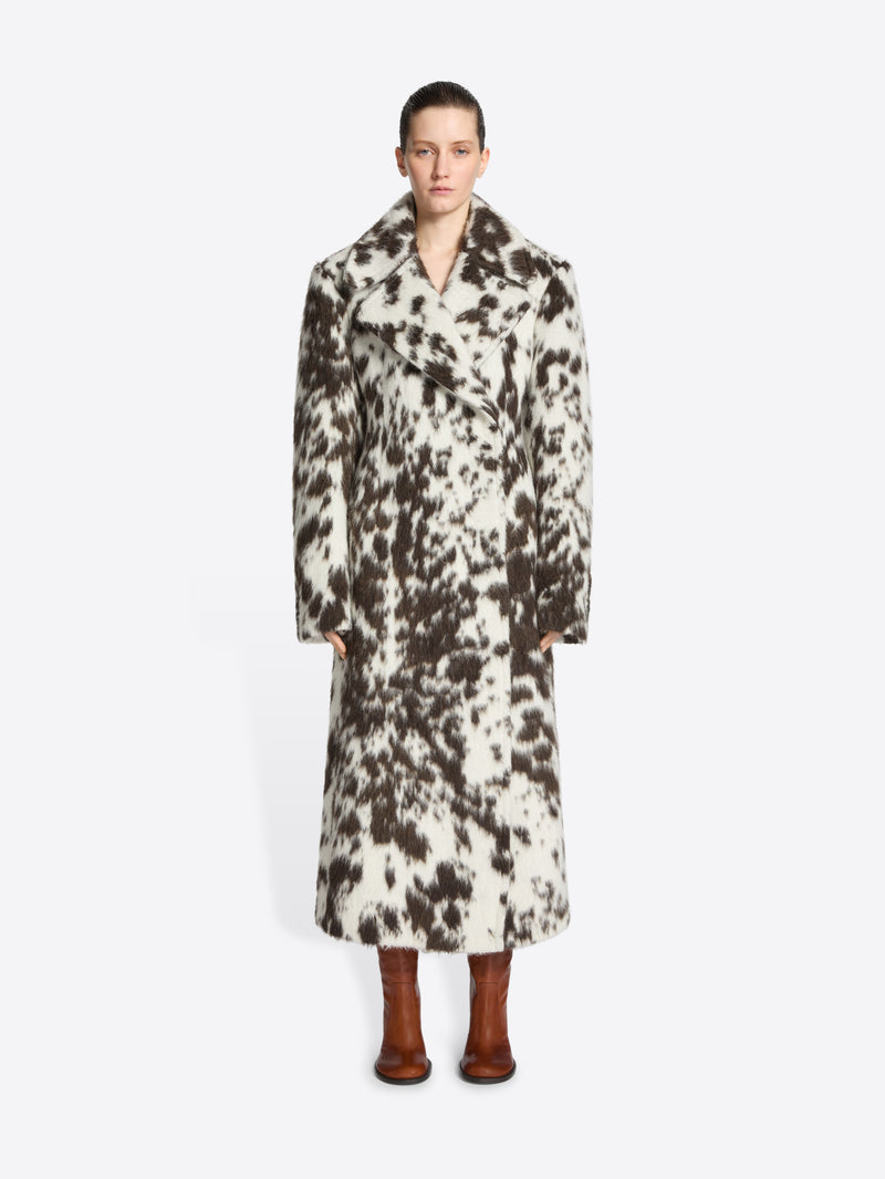 Person wearing a long brown and white spotted coat on a white background