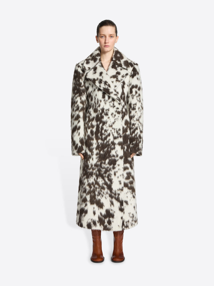 Person wearing a long brown and white spotted coat on a white background