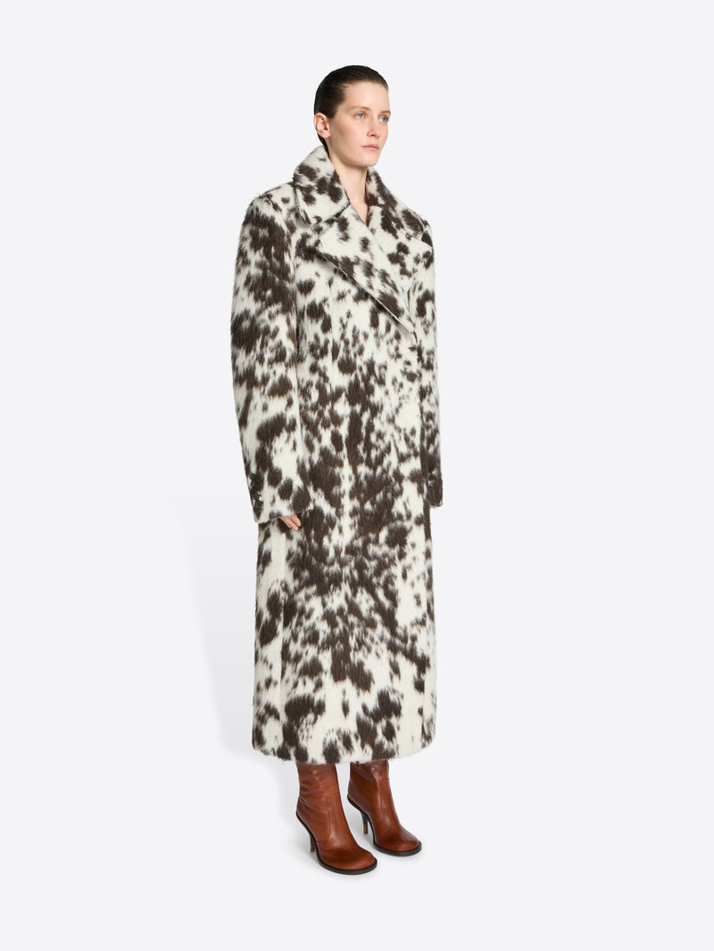 Person wearing a long brown and white spotted coat on a white background
