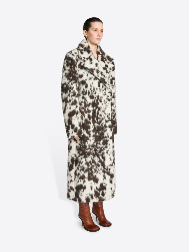 Person wearing a long brown and white spotted coat on a white background