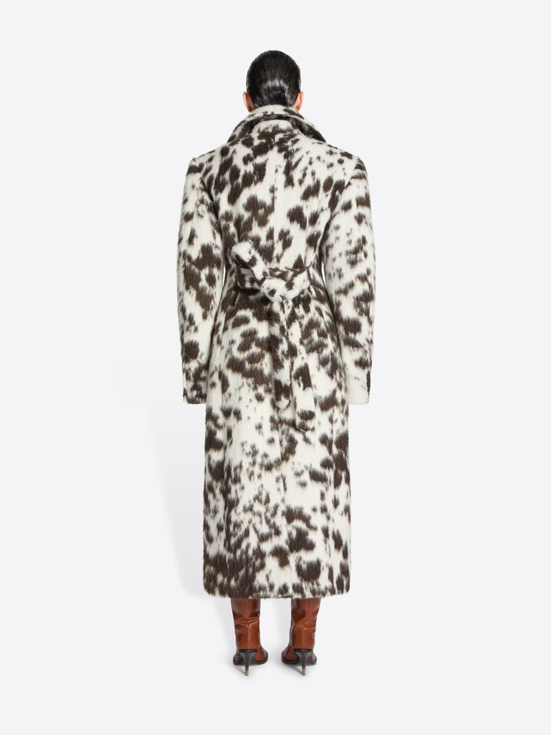 Person wearing a long brown and white spotted coat on a white background