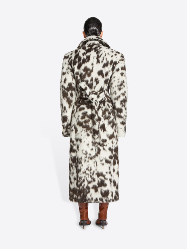 Person wearing a long brown and white spotted coat on a white background