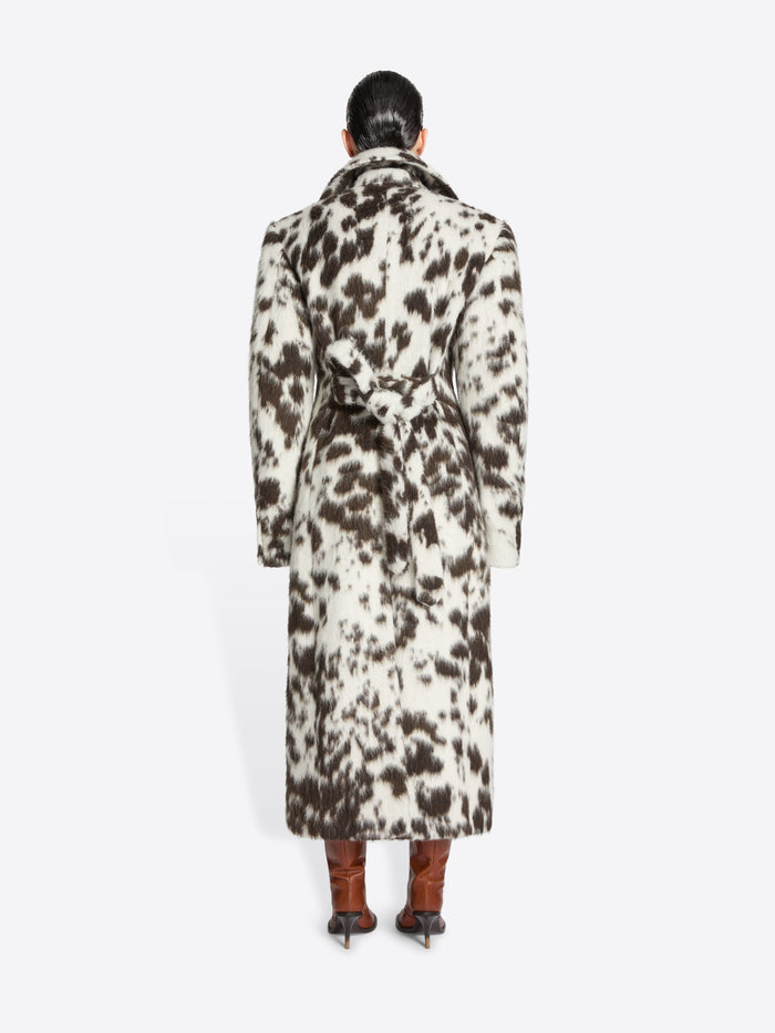 Person wearing a long brown and white spotted coat on a white background