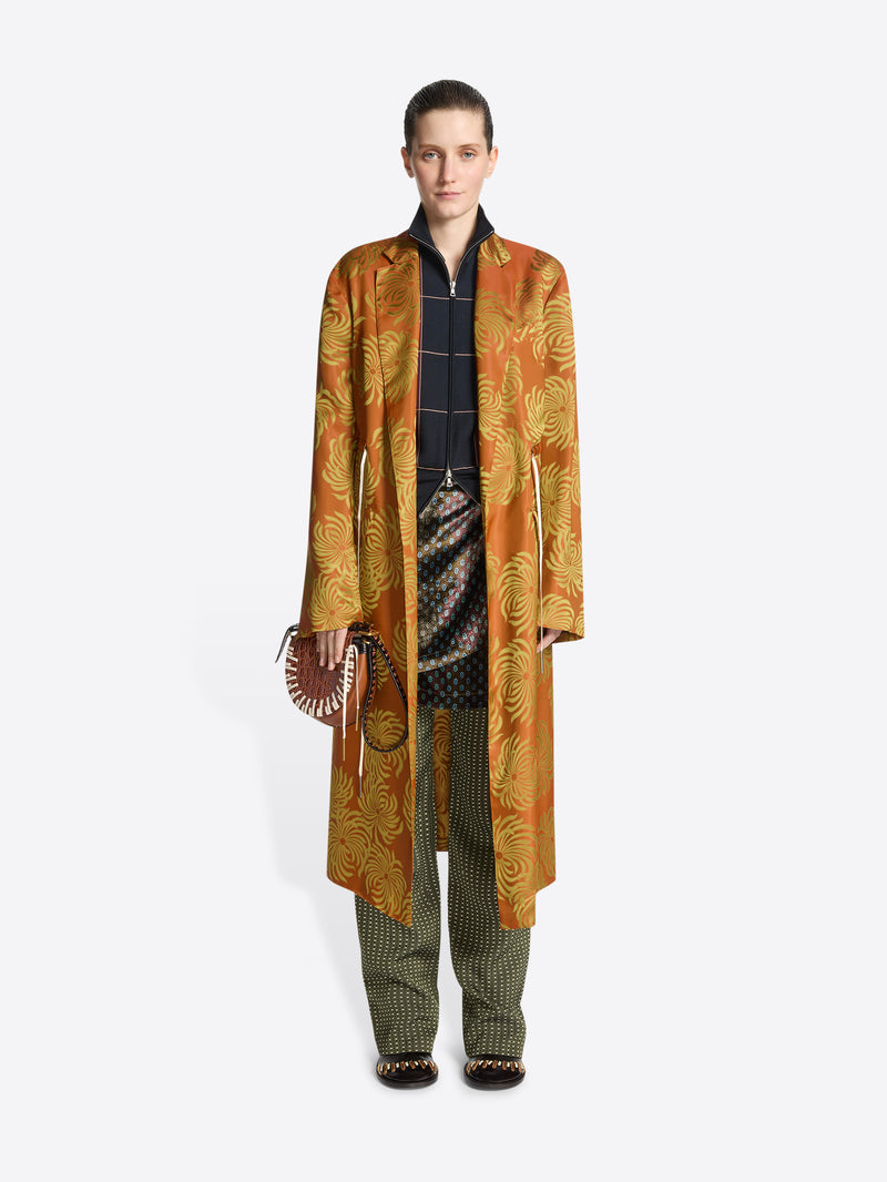 Person wearing a long orange and yellow floral print coat on a white background