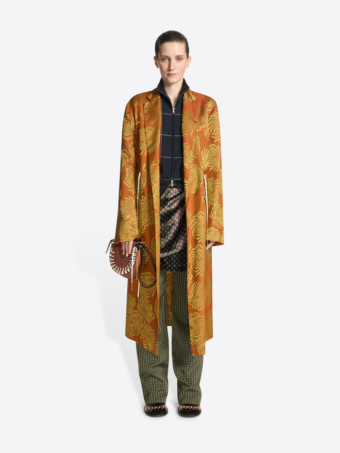 Person wearing a long orange and yellow floral print coat on a white background