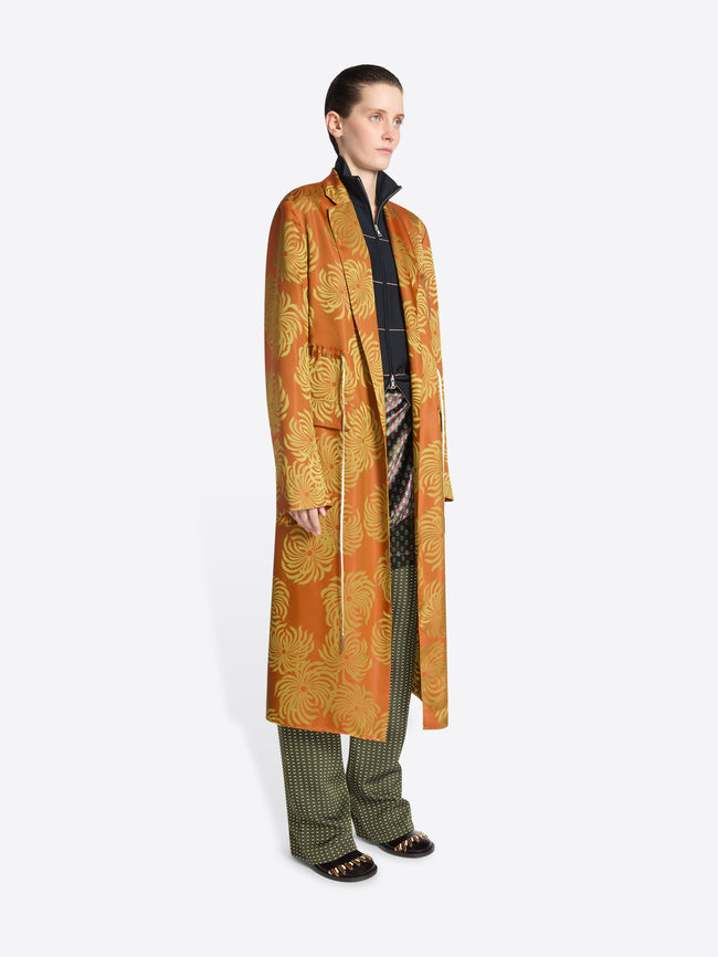Person wearing a long orange and yellow floral print coat on a white background