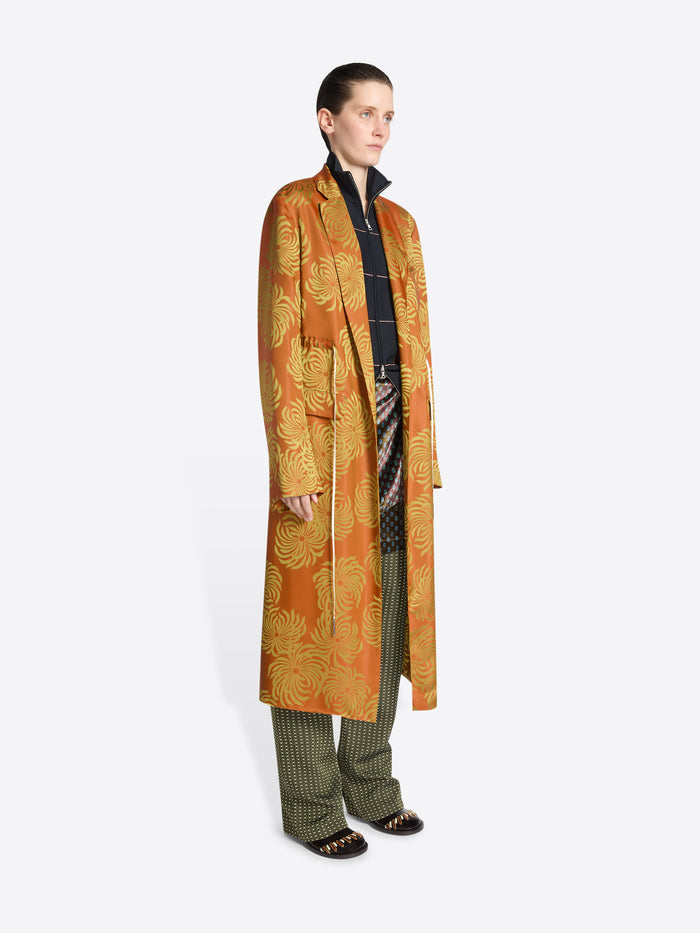 Person wearing a long orange and yellow floral print coat on a white background