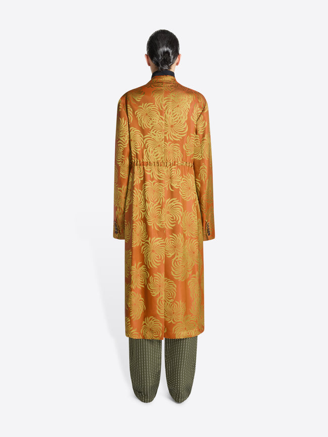 Person wearing a long orange and yellow floral print coat on a white background