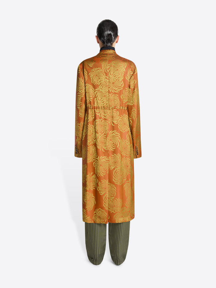 Person wearing a long orange and yellow floral print coat on a white background
