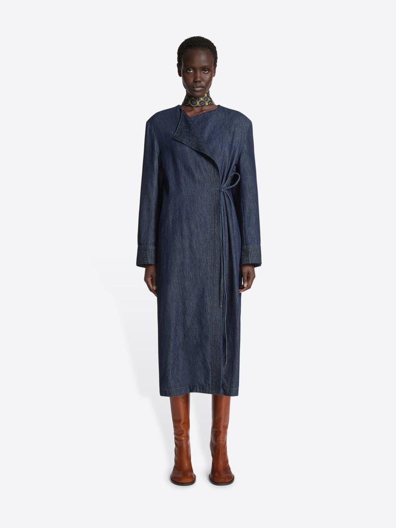 Person wearing a long collarless denim coat on a white background