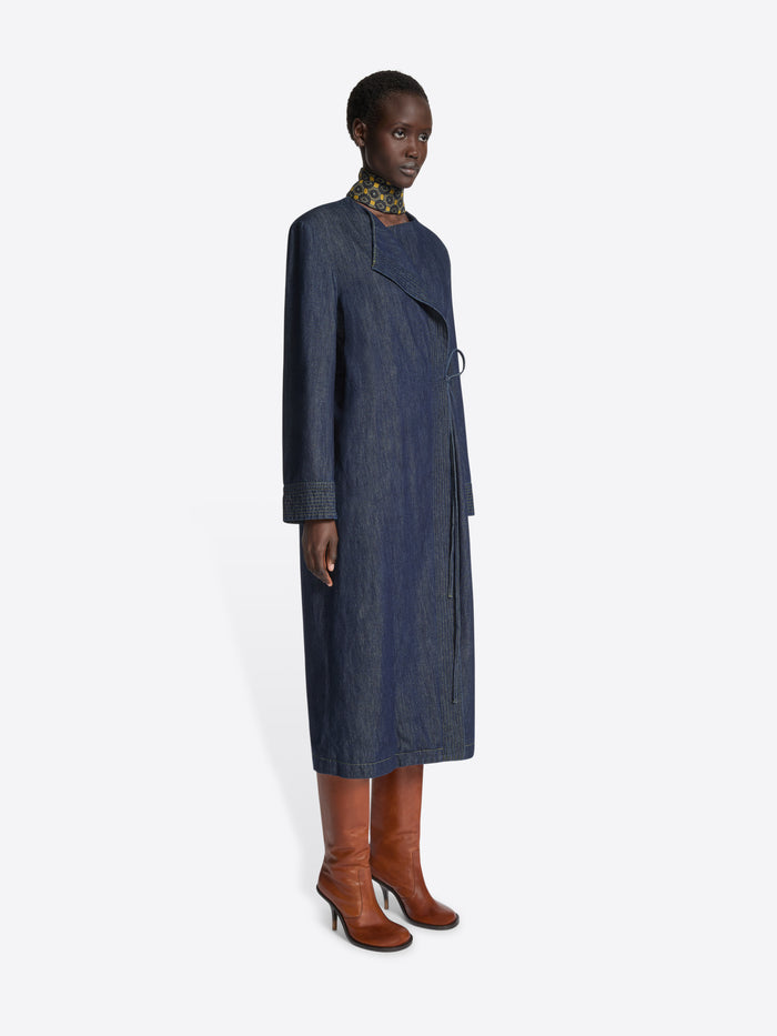 Person wearing a long collarless denim coat on a white background