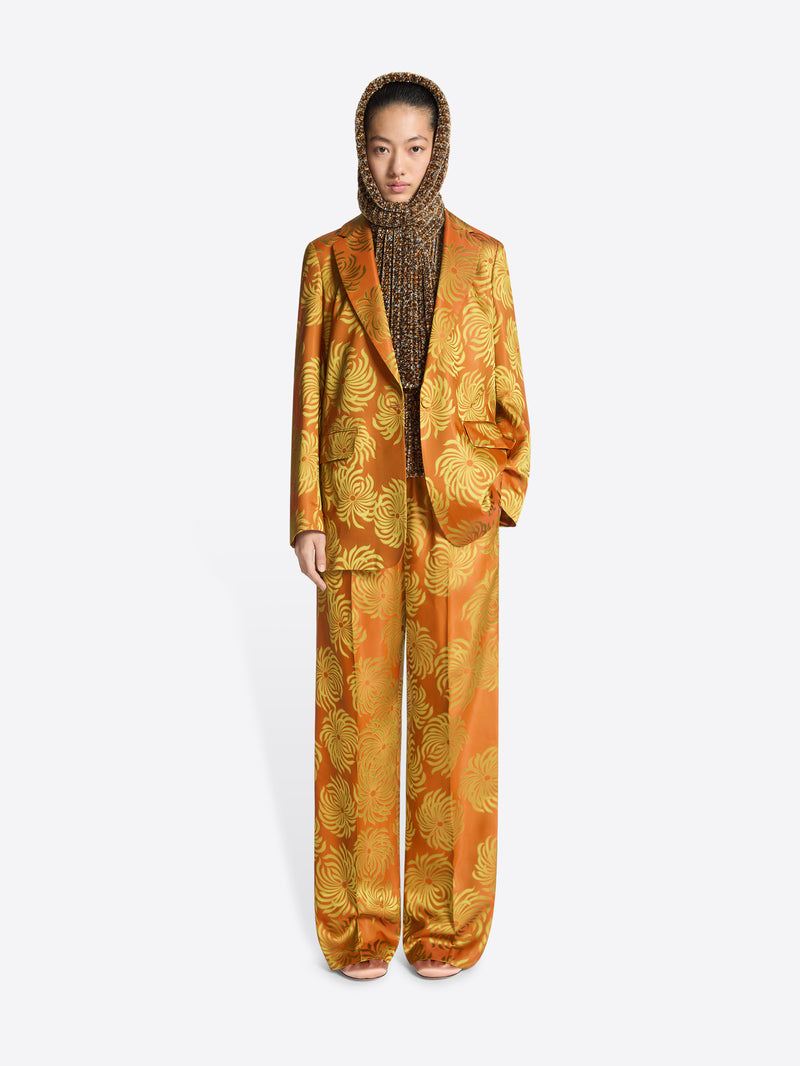 Person wearing a loose fit, orange and yellow floral jacquard blazer with matching pants on a white background