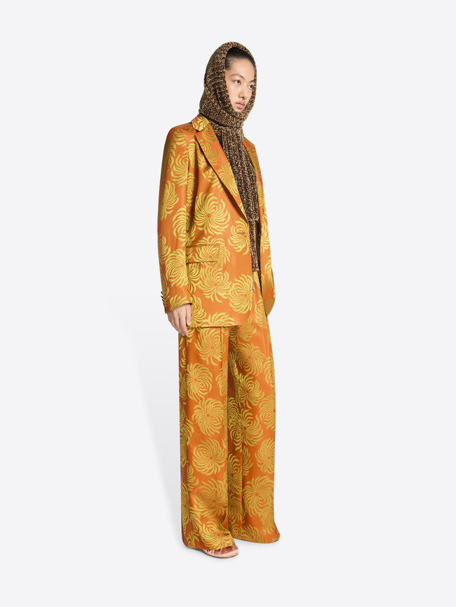 Person wearing a loose fit, orange and yellow floral jacquard blazer with matching pants on a white background