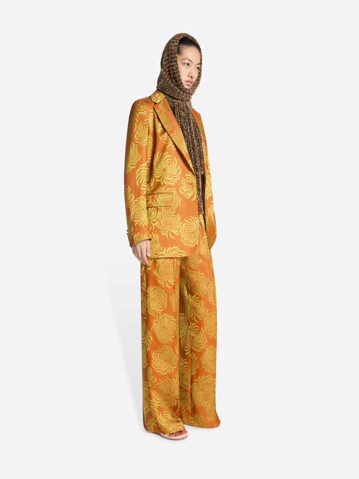 Person wearing a loose fit, orange and yellow floral jacquard blazer with matching pants on a white background