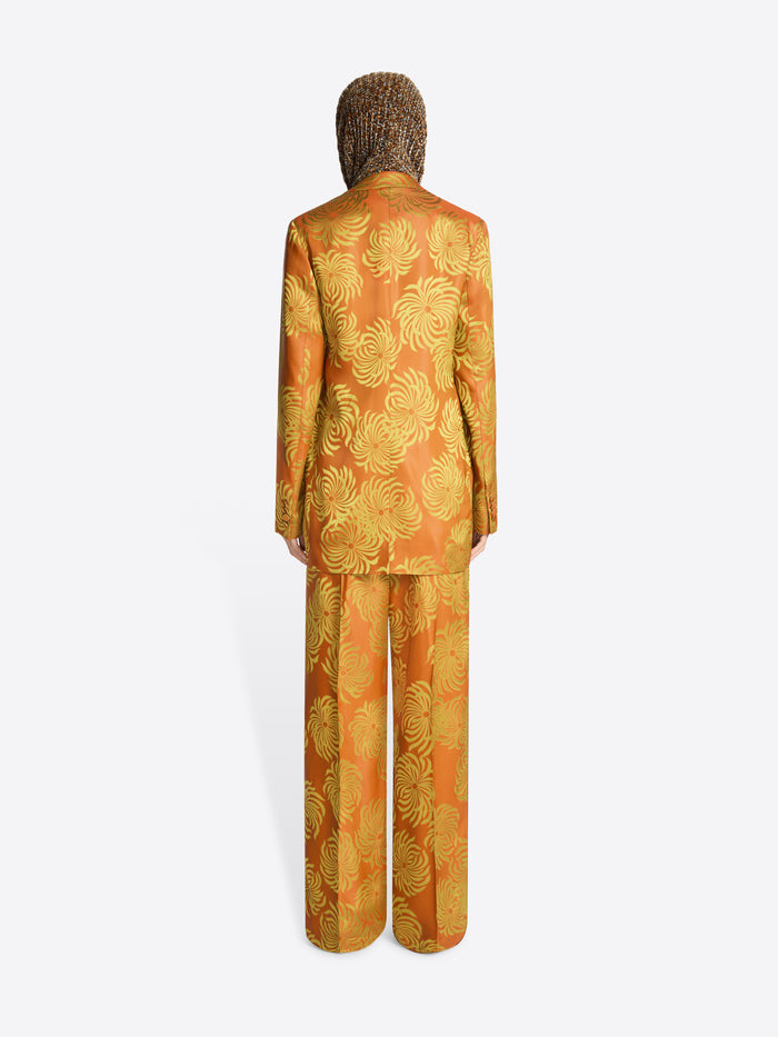 Backside of a person wearing a loose fit, orange and yellow floral jacquard blazer with matching pants on a white background