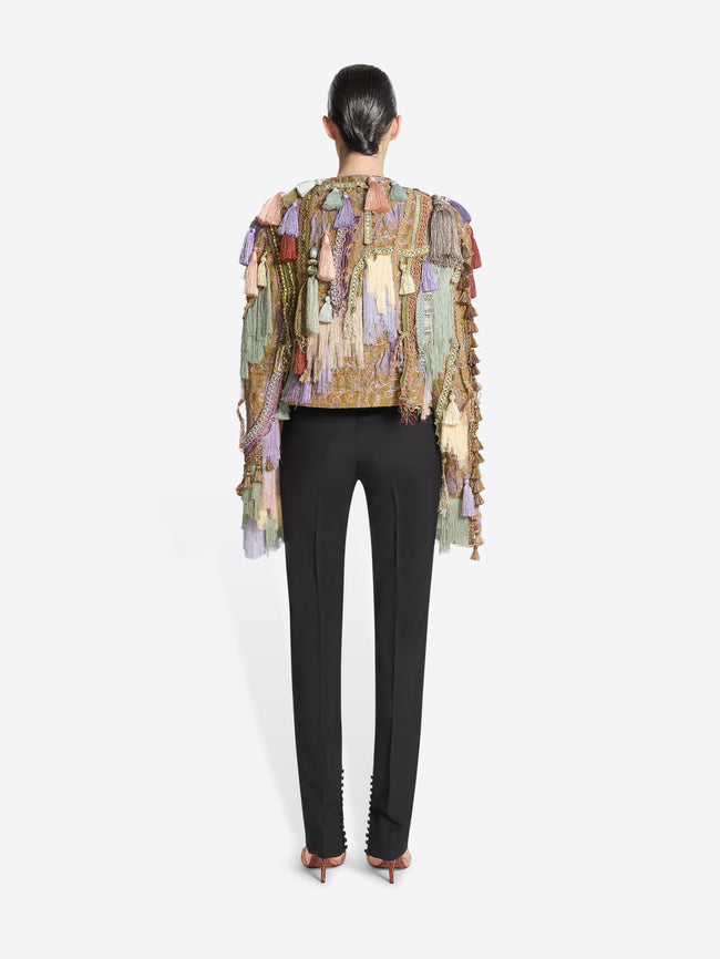Person wearing black pants and a multicolored textured jacket with tassels on a white background