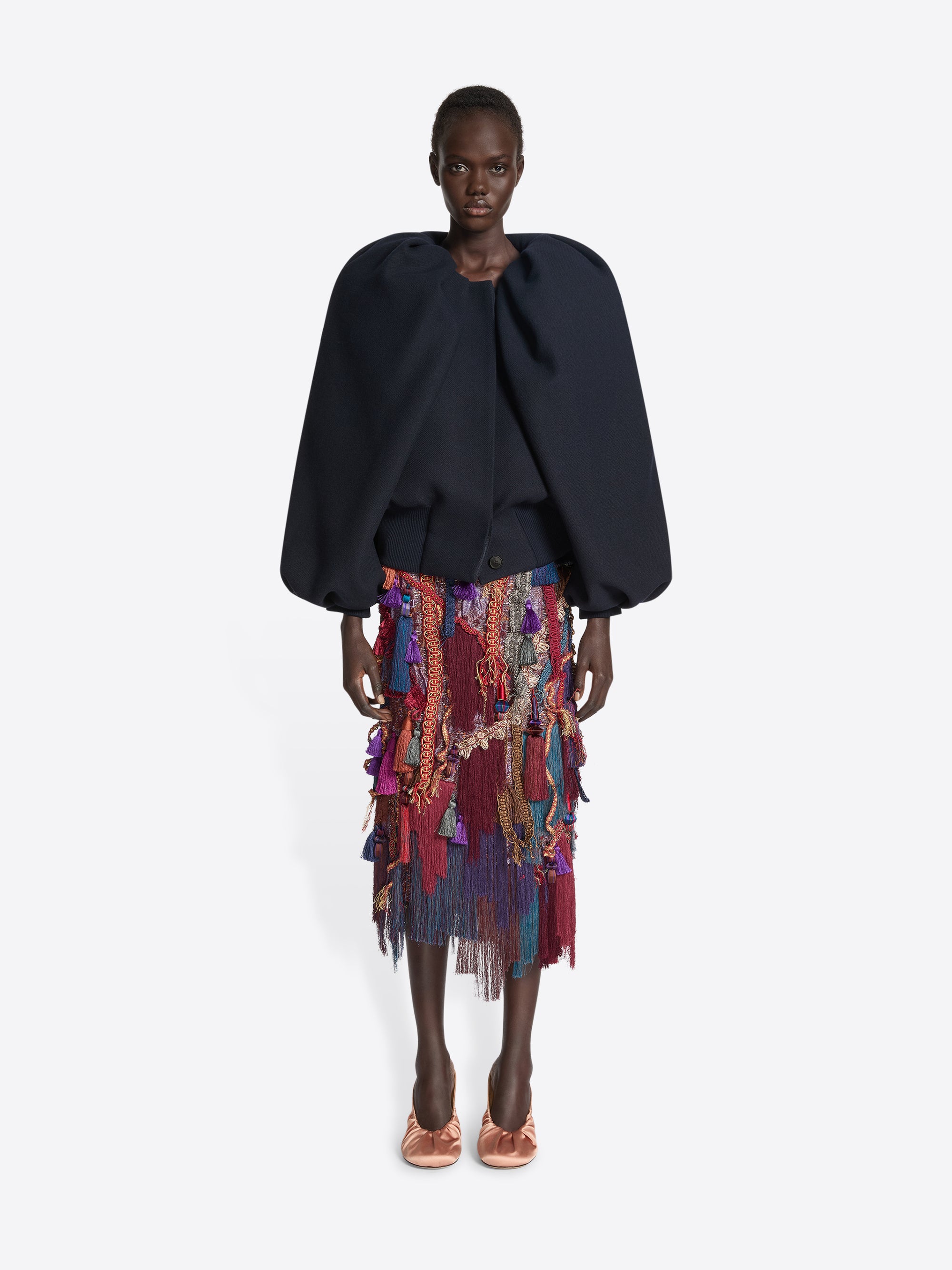 Person wearing a multi coloured skirt and navy jacket with balloon sleeves on a white background