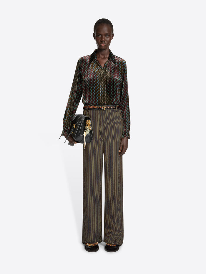 Person wearing a khaki patterned velvet shirt and brown striped pants on a white background