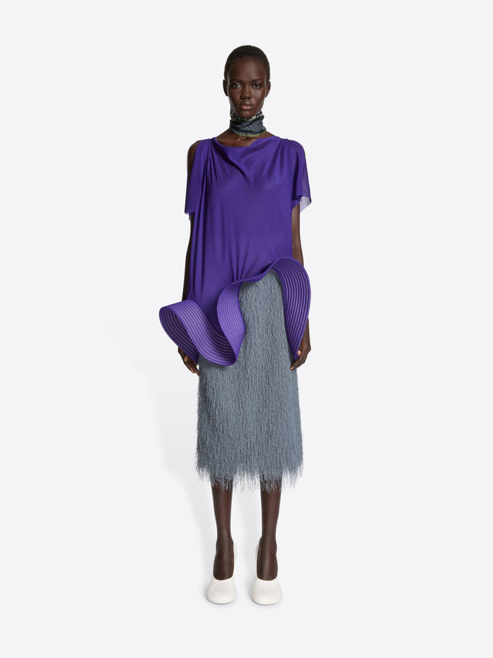 Model wearing a purple top and gray skirt on a white background