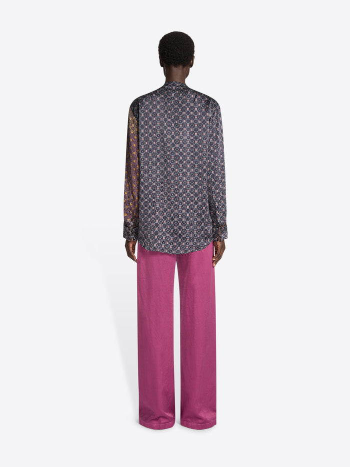 Person wearing pink pants and a multicolour patterned blouse with a tie detail on a white background