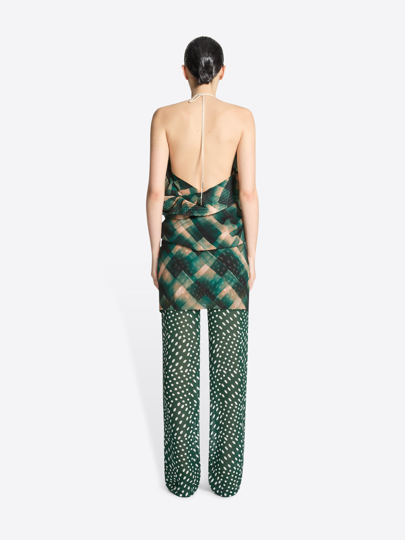 Person wearing a backless, long green and beige patterned fabric top on a white background