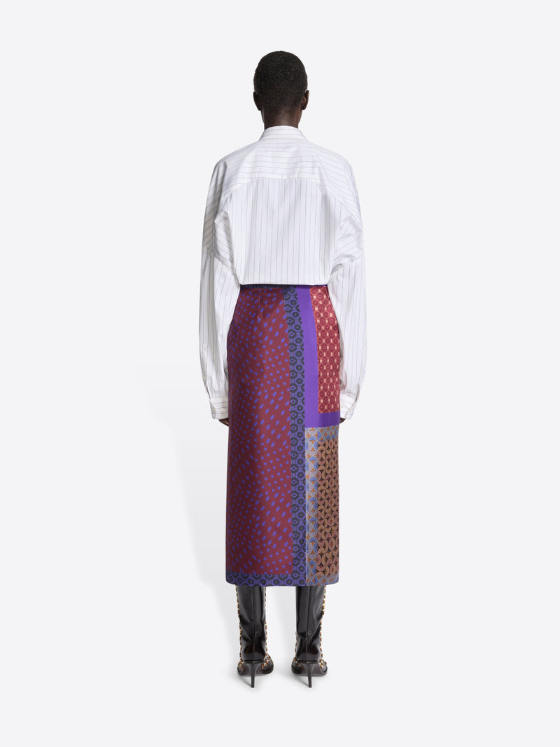 Backside of a model wearing a white shirt and multi-colored patterned skirt on a white background