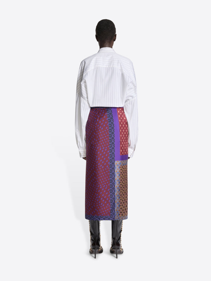 Backside of a model wearing a white shirt and multi-colored patterned skirt on a white background
