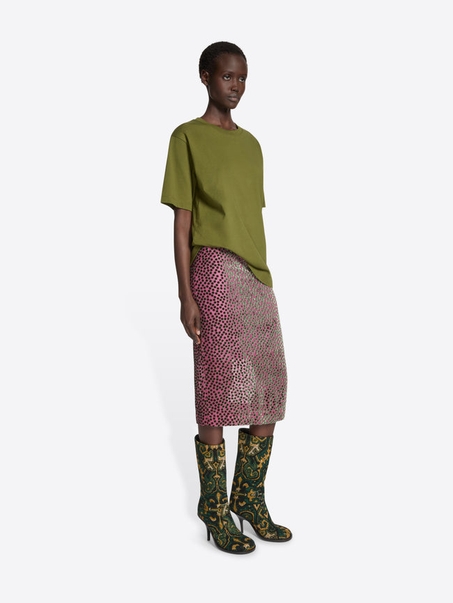 Model wearing a green top and patterned skirt with floral boots on a white background
