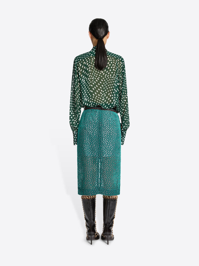 Person wearing a green patterned blouse and teal skirt on a white background