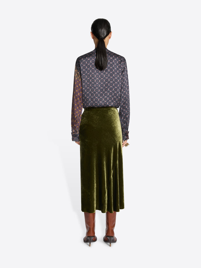 Woman wearing a patterned top and green skirt on a white background