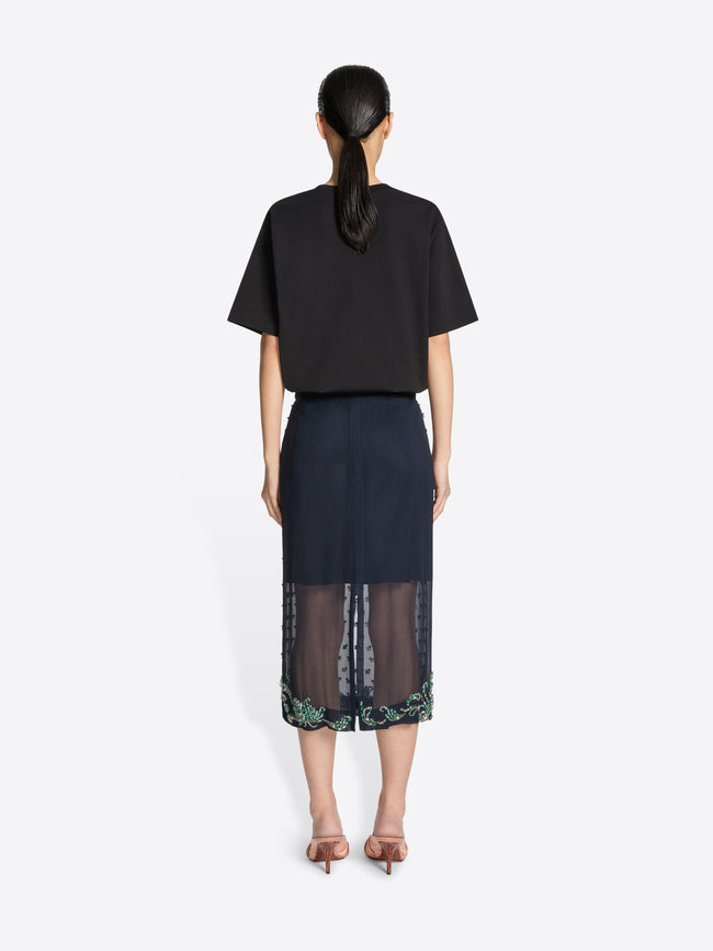 Backside of a person wearing a navy embellished skirt and a black shirt on a white background