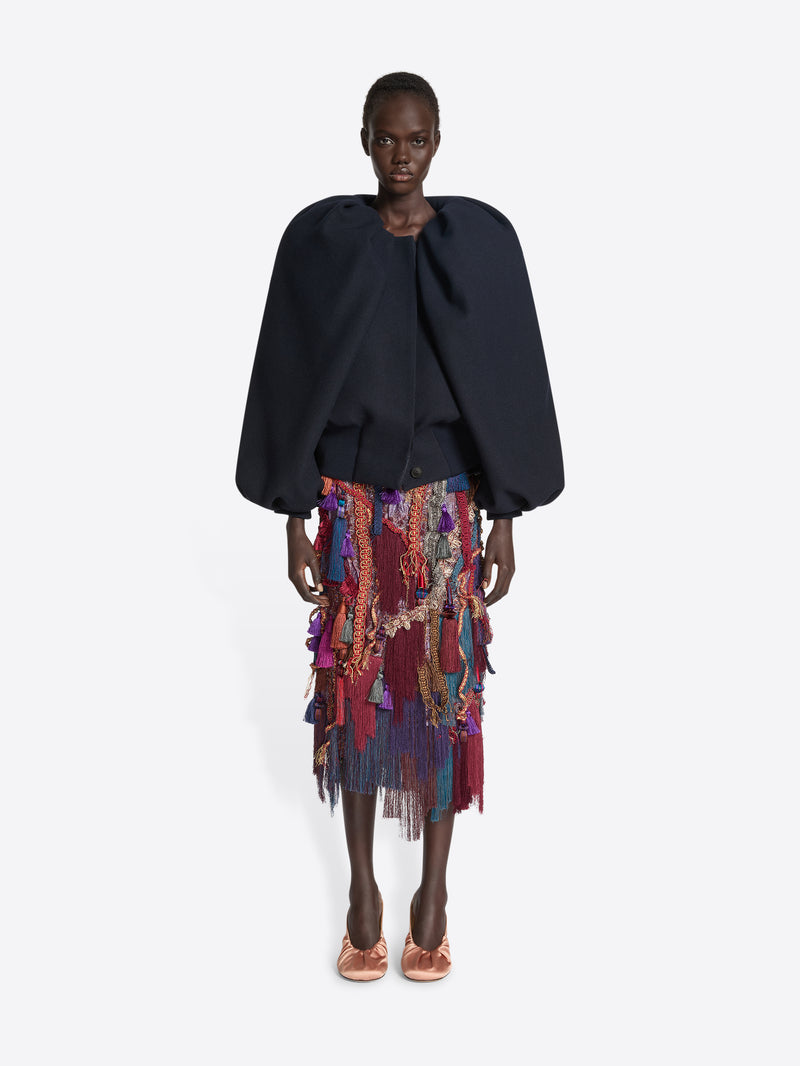 Person wearing a navy balloon top and a multicoloured, burgundy embellished skirt on a white background