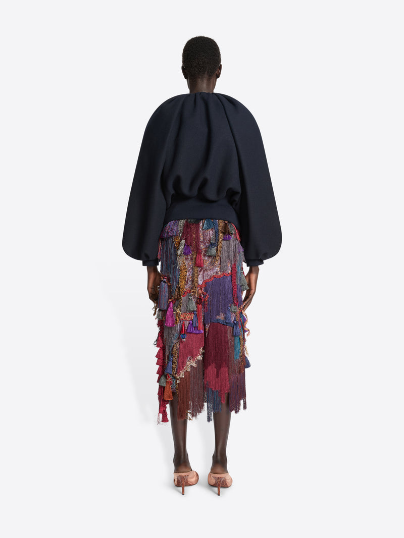 Person wearing a navy balloon top and a multicoloured, burgundy embellished skirt on a white background