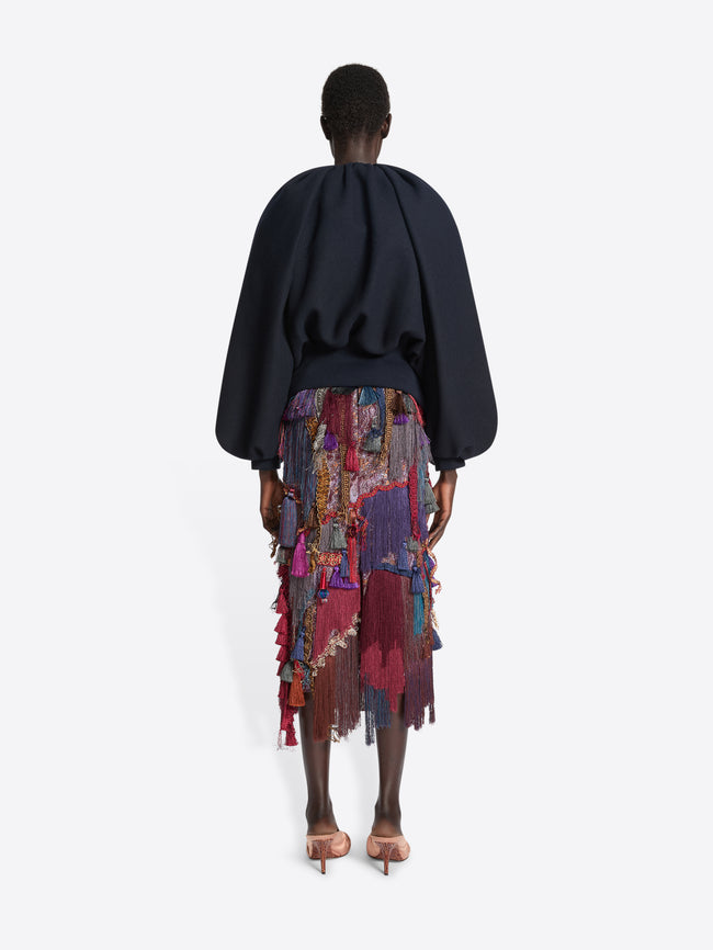 Person wearing a navy balloon top and a multicoloured, burgundy embellished skirt on a white background