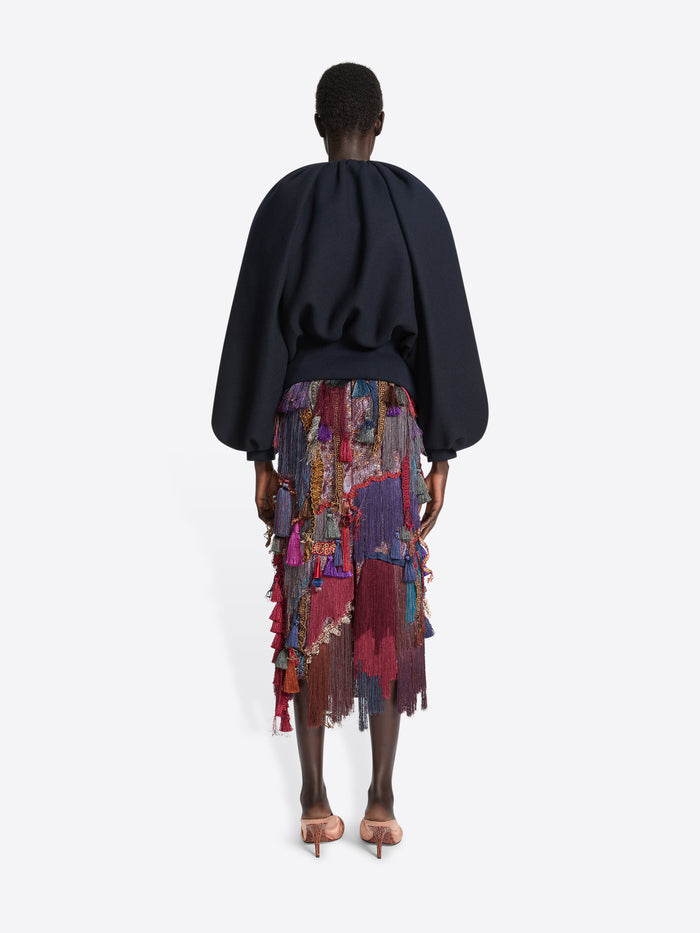 Person wearing a navy balloon top and a multicoloured, burgundy embellished skirt on a white background